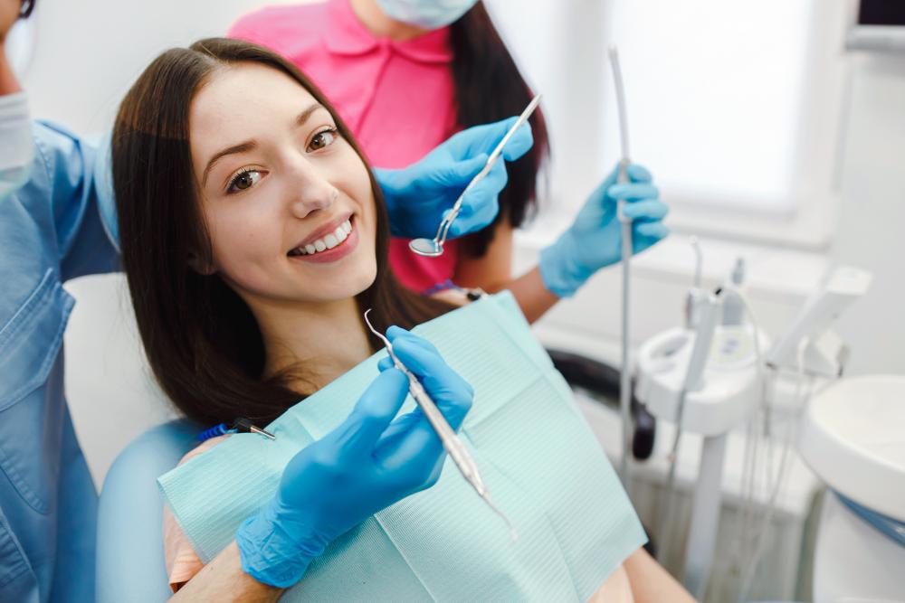 a woman on the dental chair smiling with hands holding some dental tools